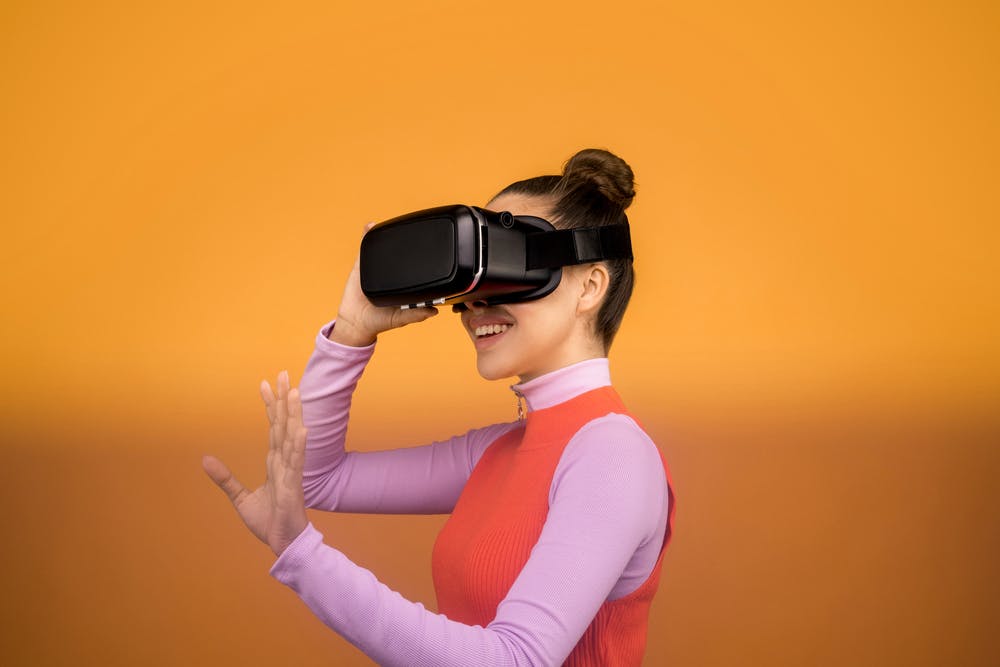 Imagen de una mujer joven sonriendo, situada de perfil, utilizando unas gafas de realidad virtual realizando movimiento con las manos.